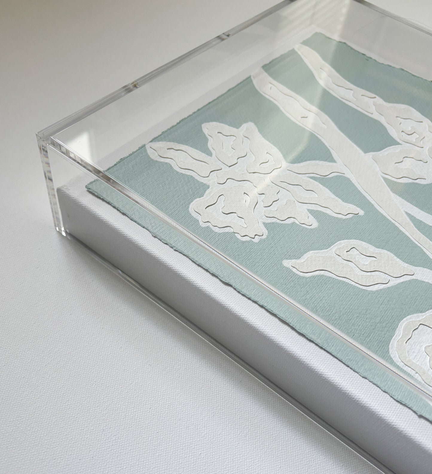 Framed botanical collage by Kendal Blanchard Art with white floral patterns on cotton rag in a clear acrylic box frame.