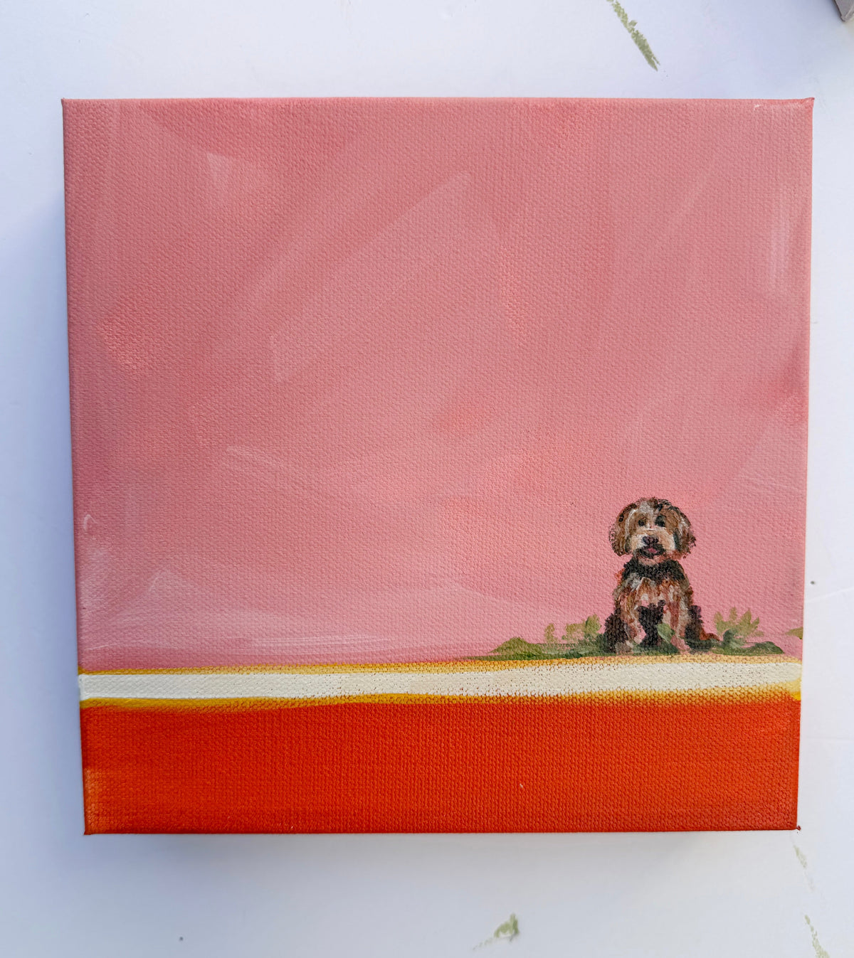 A small labradoodle painting of a dog sitting in grass against a pink sky above an orange horizontal stripe.