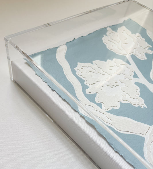 Layered botanical collage by Kendal Blanchard Art with white florals on cotton rag paper, in a clear acrylic box frame.