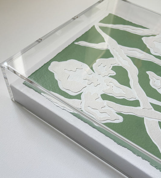 A green and white botanical collage by Kendal Blanchard Art, on cotton rag in an acrylic frame, rests on a white surface.
