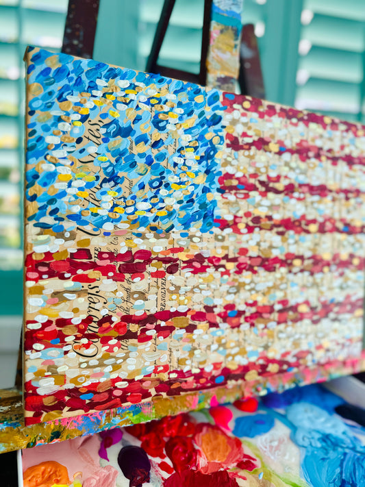 Acrylic American flag painting by Lauren Marshall Fine Art on easel, palette with paint blobs below.