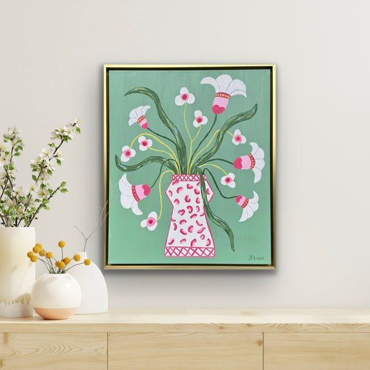 Jeanne Player’s original acrylic painting of white flowers in a pink vase on green, displayed on a wooden shelf.