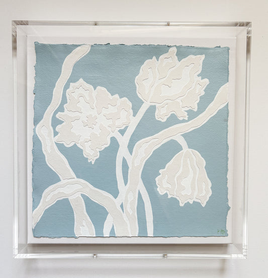 A botanical collage by Kendal Blanchard Art features abstract white flowers on blue, framed in an acrylic box frame.