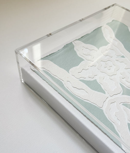 A framed abstract by Kendal Blanchard Art with white textured shapes on handmade cotton rag in a clear acrylic box frame.