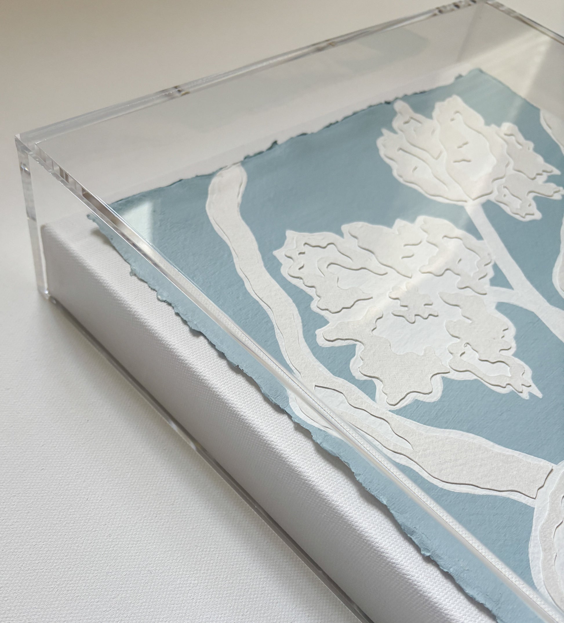 Handmade cotton rag paper floral cutouts on blue, framed in clear acrylic by Kendal Blanchard Art for a bold collage.