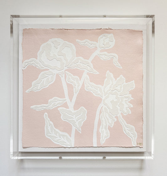 Kendal Blanchard Art botanical collage of two abstract white flowers with leaves, in an acrylic box frame on a white wall.