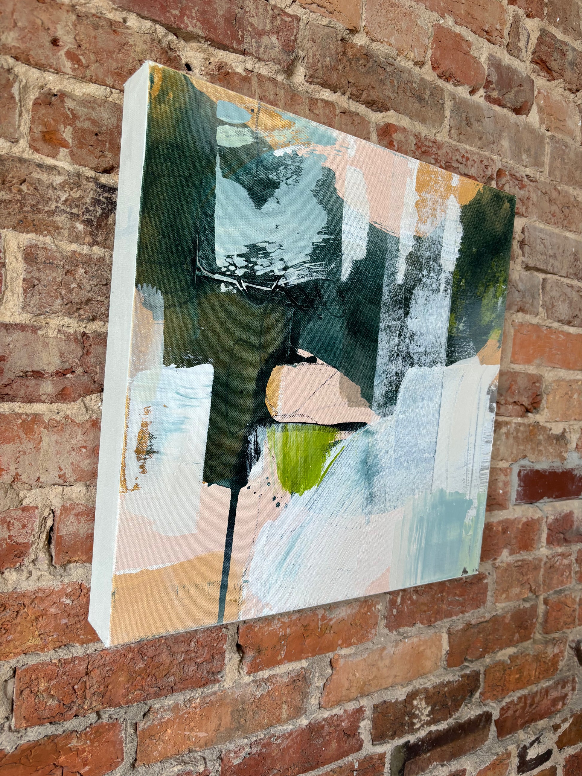 Emily Pullin mixed media canvas art with green, white, black & peach shapes displayed on a rustic brick wall.