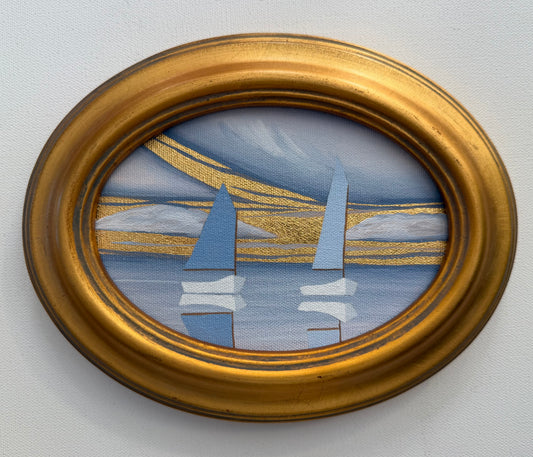 Oval coastal artwork of two sailboats on water with gold-leaf clouds in a metallic gold frame.