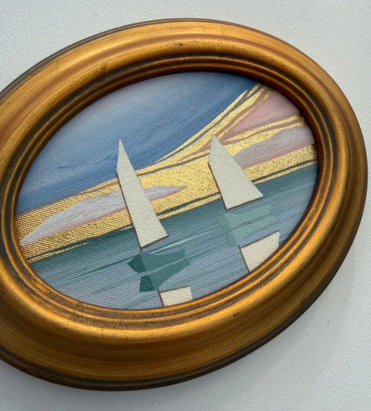 Oval Nikki Storer coastal artwork of sailboats on water with gold leaf accents in a gilded frame.