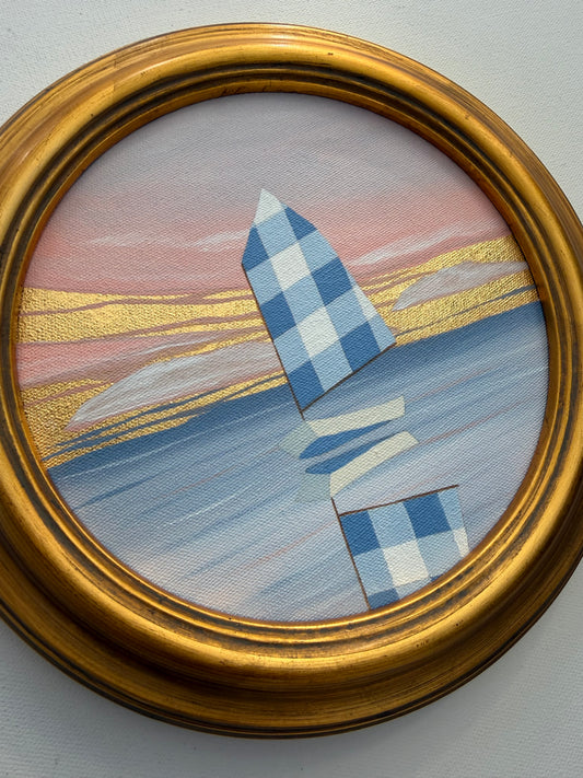 A circular coastal artwork of a blue checkered sailboat on water with 24K gold leaf accents, encased in a gold frame.