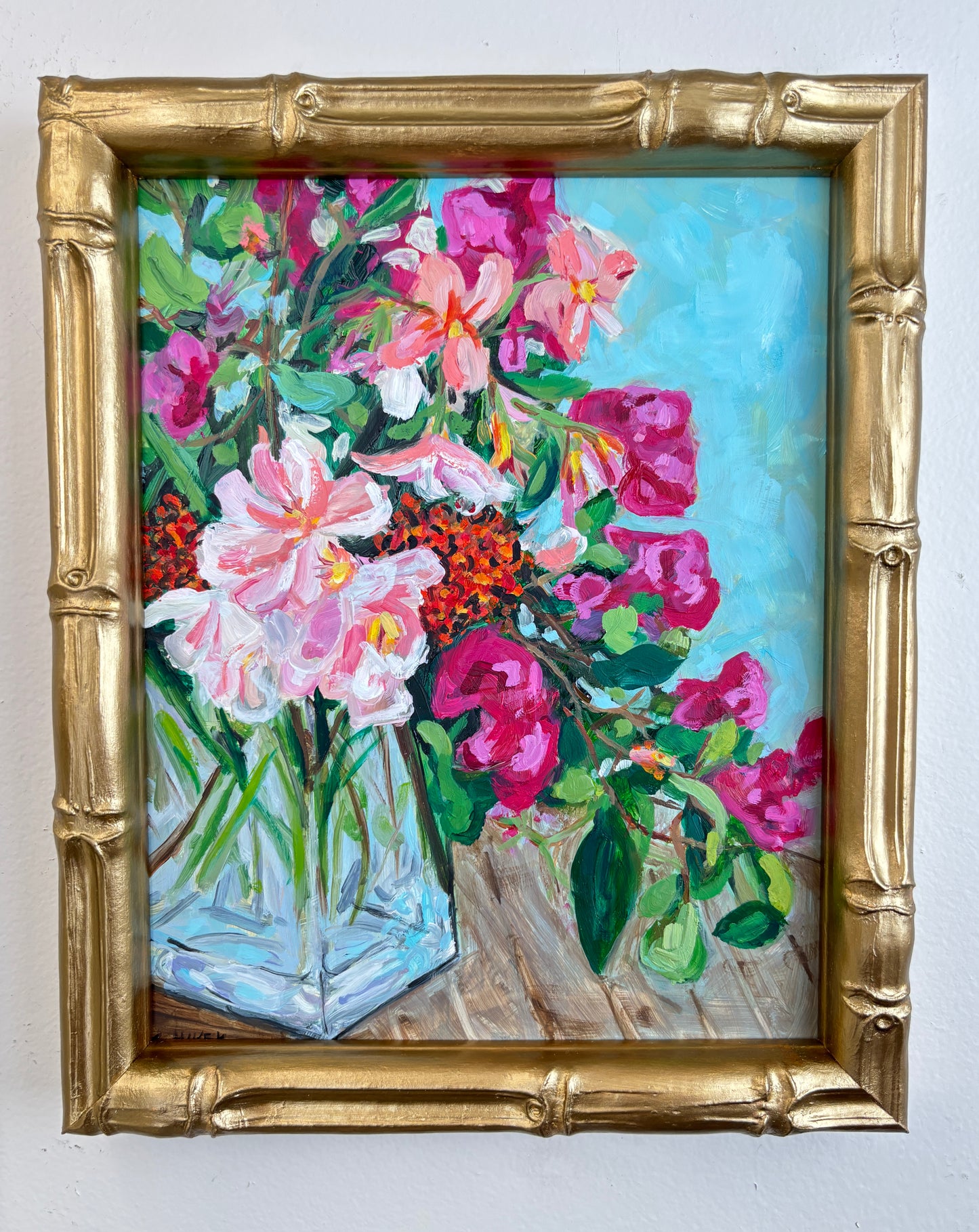 Catherine Husek’s framed floral art with pink and red flowers in a vase, in a gold bamboo-style frame on a light wall.
