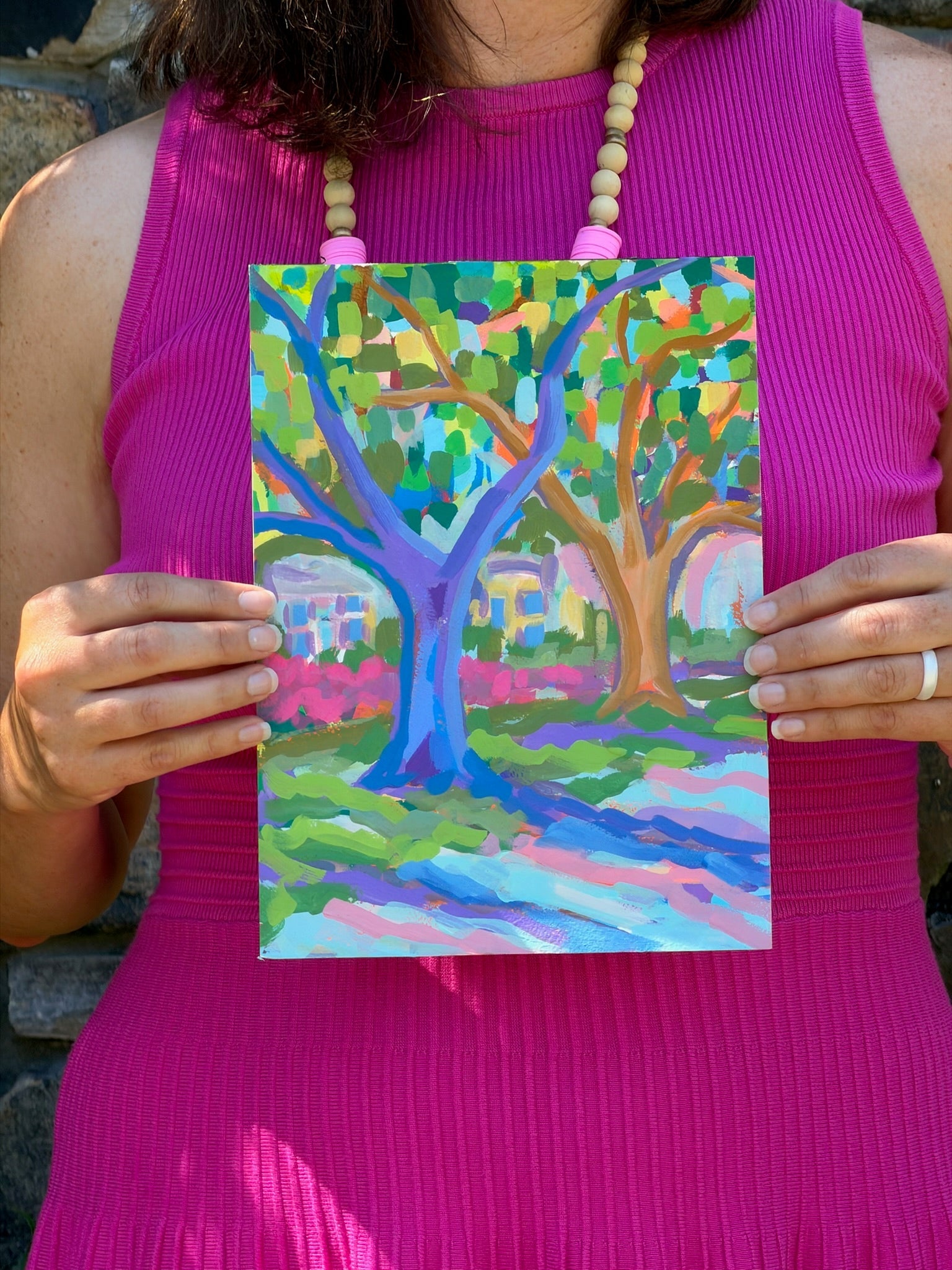 A woman in a pink dress holds original watercolor art from Elizabeth Sheats Art & Design, featuring two vibrant trees.