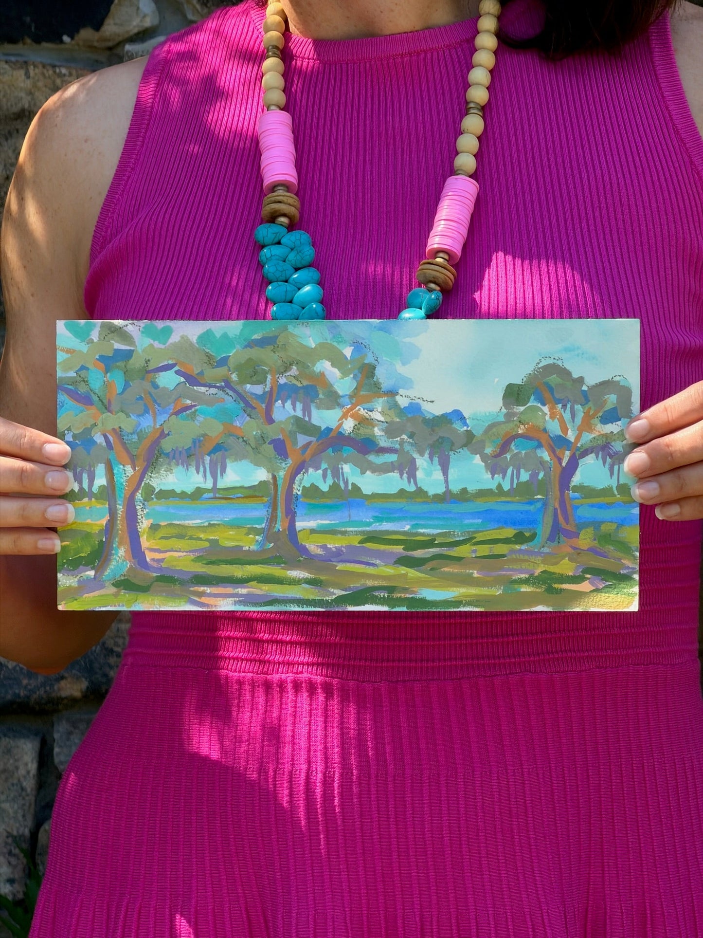 A person in a pink dress holds an original live oak tree painting by Elizabeth Sheats Art & Design.