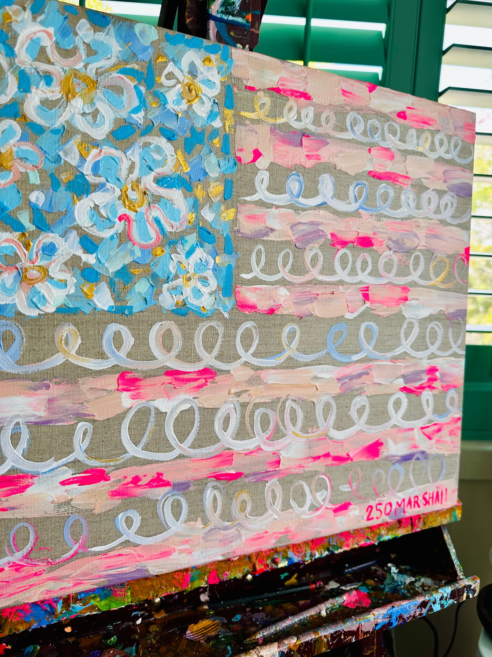 A Lauren Marshall Fine Art abstract flag painting with pastel swirls and florals on canvas, displayed on an easel.