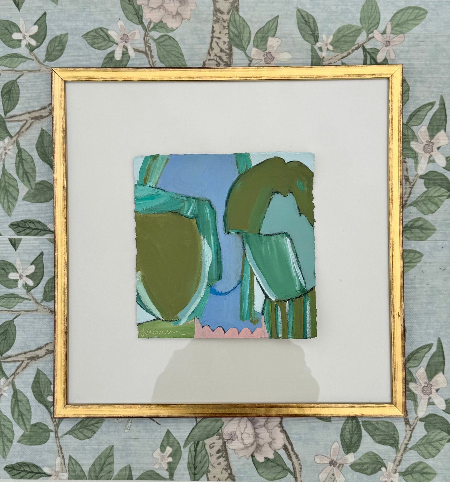 Abstract green and blue mixed media painting by KP Art Collective in a gold frame, displayed on floral wallpaper.