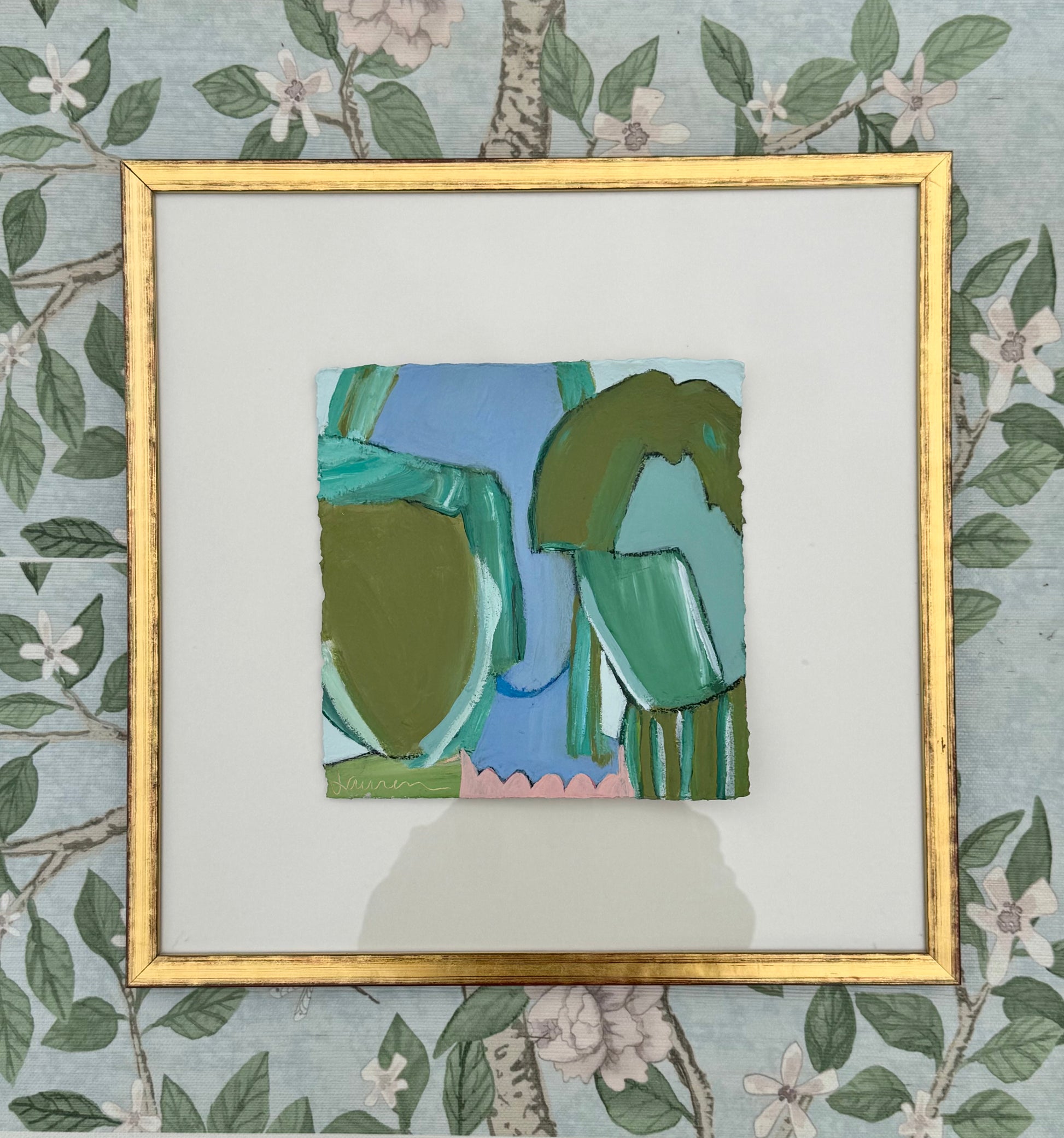 Abstract green and blue mixed media painting by KP Art Collective in a gold frame, displayed on floral wallpaper.