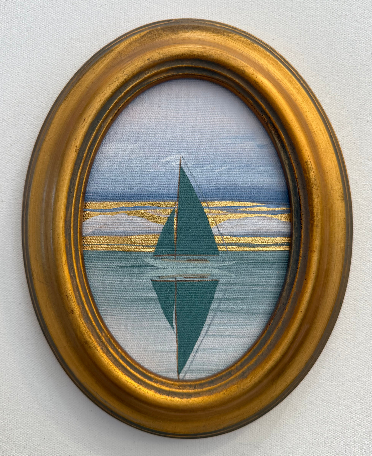 Oval Nikki Storer painting of a teal sailboat reflecting on calm water, accented with horizontal gold-leaf bands.