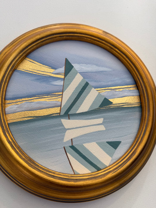 A round 24K goldleaf painting of a sailboat with blue and white striped sails against a sky with gold horizontal lines.