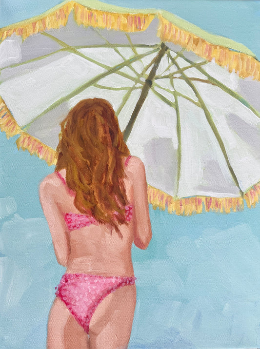 A woman in a pink bikini stands beneath a fringed beach umbrella—perfect beach art or wall decor under clear blue skies.