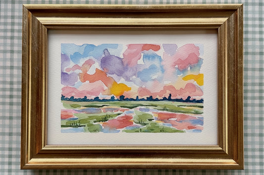 Framed watercolor painting of a colorful landscape with a gold frame on a checkered background.