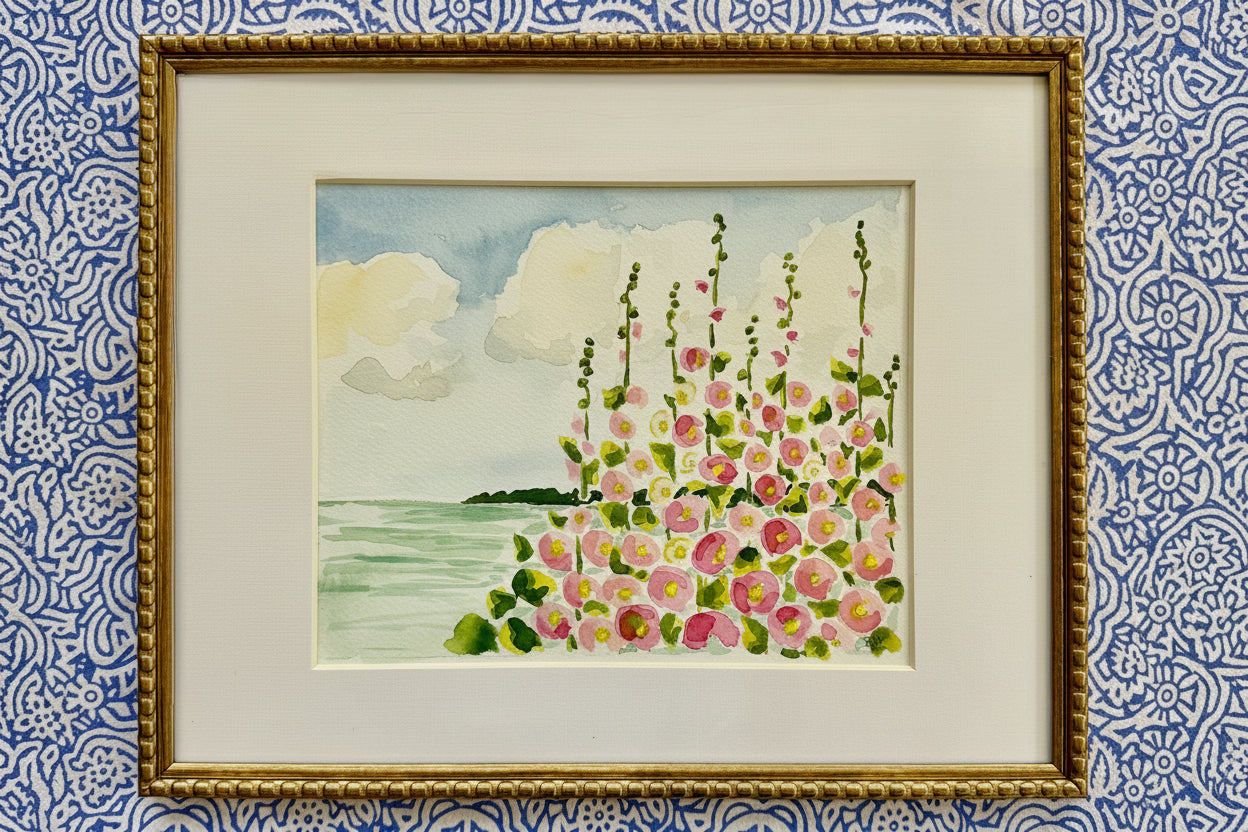 S Jane Hamilton watercolor: pink hollyhocks by water, clouds, greenery, 12x15 framed, blue patterned wallpaper.
