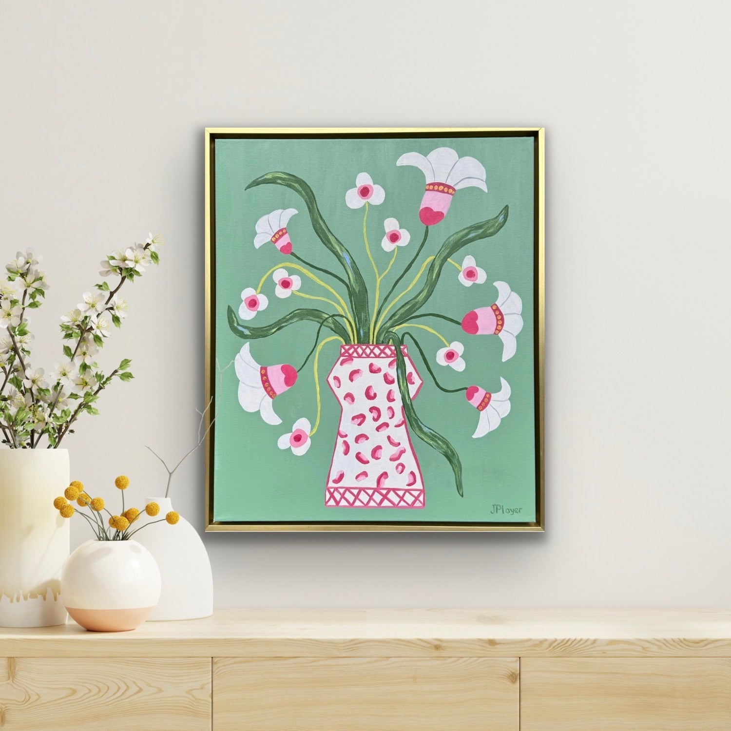 Jeanne Player’s original acrylic painting of white flowers in a pink vase on green, displayed on a wooden shelf.
