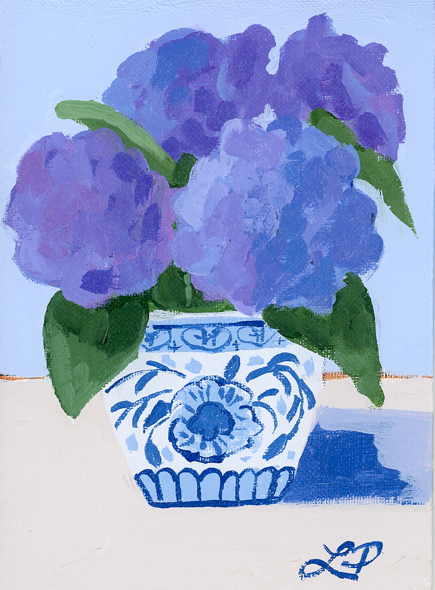A Lauri Prins blue and white vase holds purple hydrangeas with green leaves for striking floral home decor.